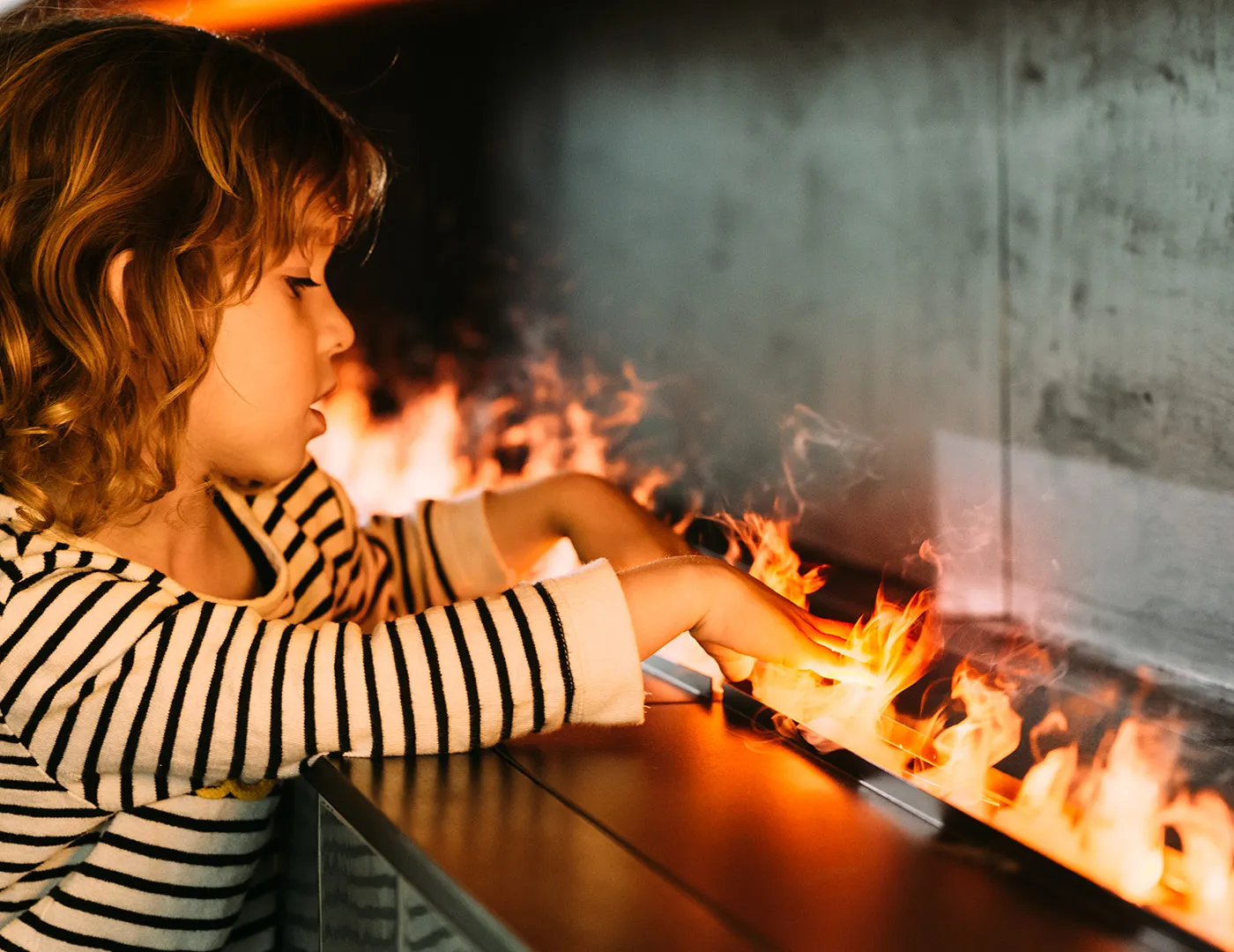 Lille pige stikker fingrene ind i flammerne fra en vanddamp-pejs